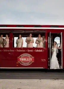 bride holding up a bouquet as she boards a red trolley with bridesmaids posing by the windows onboard.