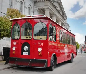 Front view of a classic red trolley infront of a large limestone building in Kingston Ontario.