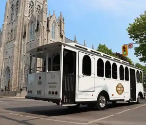 White trolley driving past a large limestone cathedral