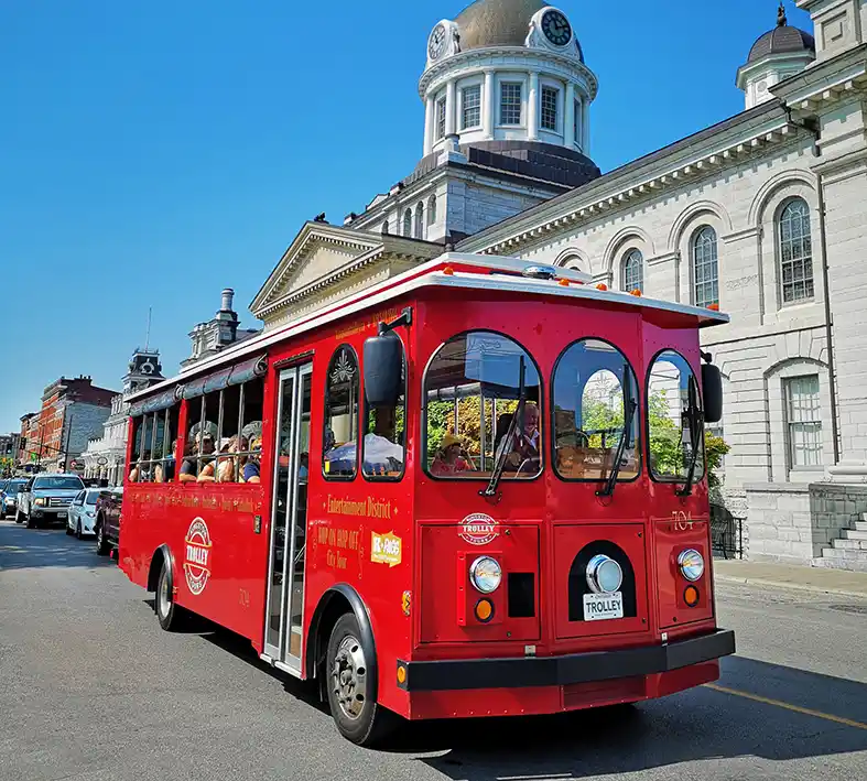 Red Trolley driving past City Hall a large limestone building in downtown Kingston, Ontario