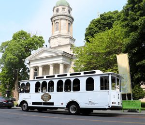 White trolley passing by St. Andrews Church, a large, limestone cathedral in Kingston, Ontario.