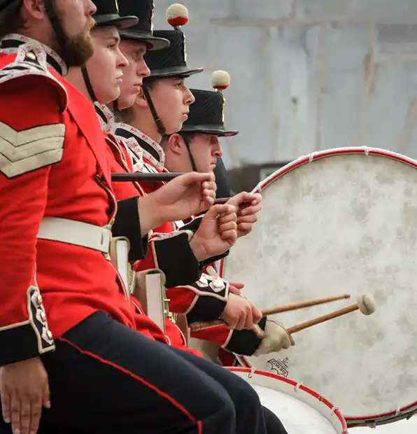 Men in blacj and red old fashioned army uniforms playing the drum at Fort Henry.